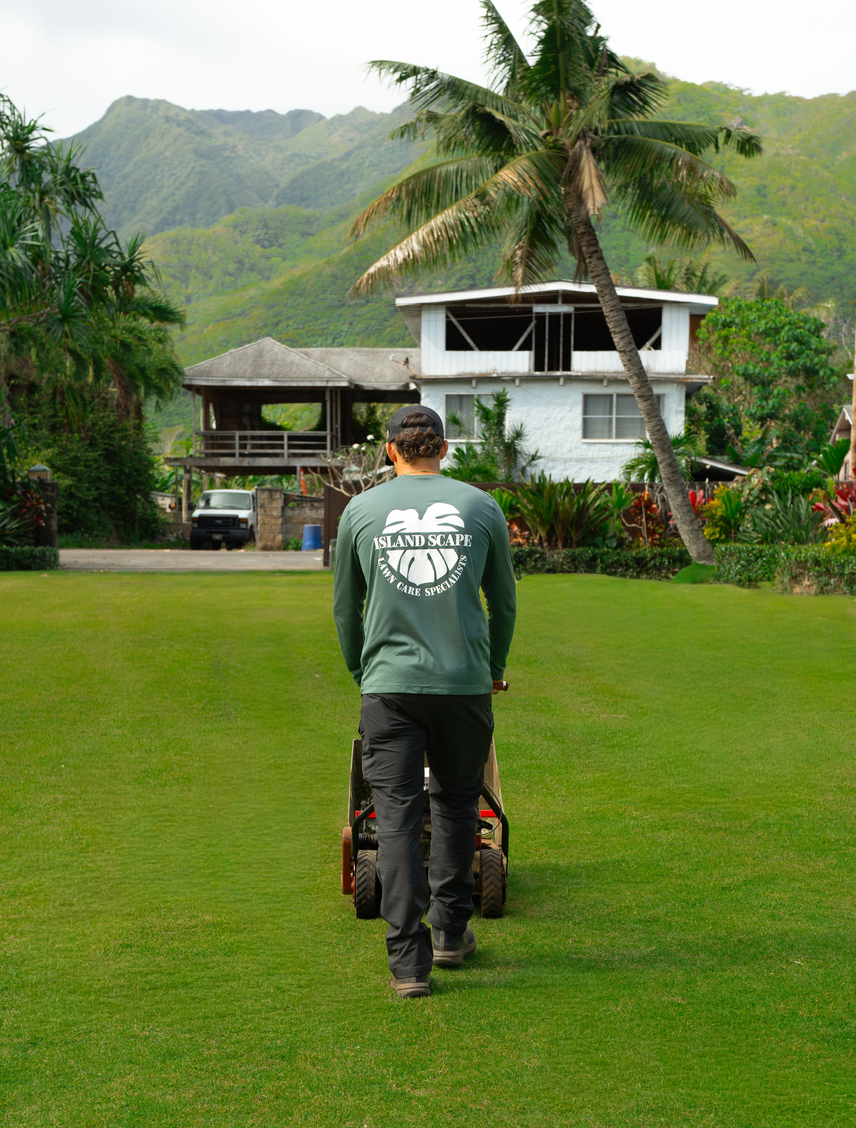 Island Scape technician mowing a lush North Shore lawn with Ko'olau mountains in the background